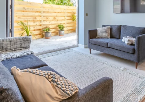 Carlyon Bay Lodge, Carlyon Bay is a beautifully presented modern annexe designed for romantic escapes, featuring a light-filled open-plan interior, peaceful patio with outdoor dining, and upstairs bedroom with sweeping rooftop views towards the sea.