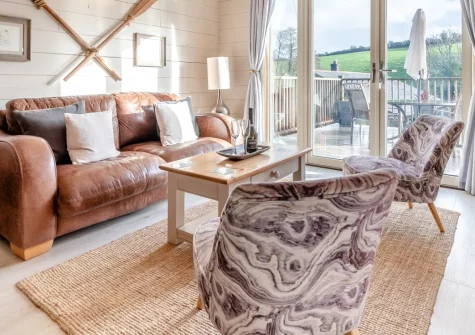 Honey Honey, Little Petherick is a charming Canadian-style log cabin near Padstow, boasting a balcony with countryside views, cosy wood-clad interiors, and a sunny decked terrace perfect for alfresco dining and relaxed Cornish holidays.