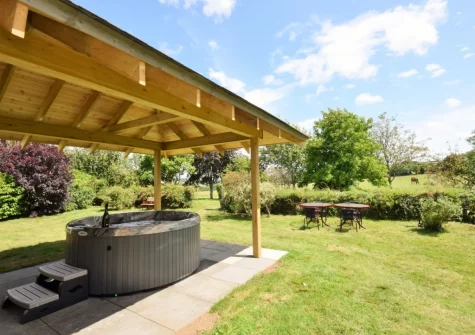 The patio, covered hot tub & large lawned cottage garden at Pendavey Lodge, Sladesbridge