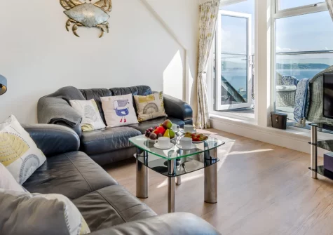 Penthouse at Lemain Garden Apartments, Looe is a contemporary second-floor retreat elevated above Looe Bay, featuring a private balcony with sea views, bright Velux-lit interiors, and easy access to East Looe's harbourside charm and sandy beaches.