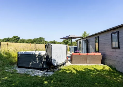 The hot tub & alfresco dining area, with views over the fields, at Violet Lodge, 11 Roadford Lake Lodges, Broadwoodwidger