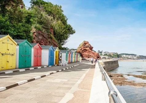 The colourful beach huts at Coryton Cove are a charming, brightly painted row nestled against steep, dramatic red cliffs